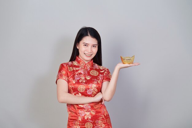 Happy Chinese new year. Portrait beautiful young asian woman wear chinese dress holding gold ingots isolated in gray studio background