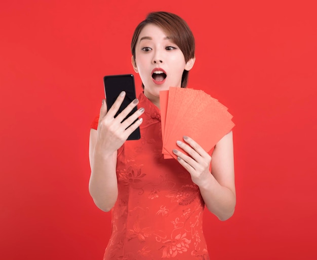 Happy chinese new year suprised young Woman holding Red envelopes for lucky and watching the mobile phone