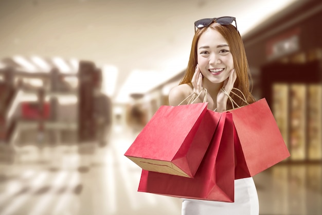 Happy chinese woman with red paper bags on the mall