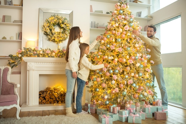 Buon natale. giovane famiglia carina che decora insieme l'albero di natale