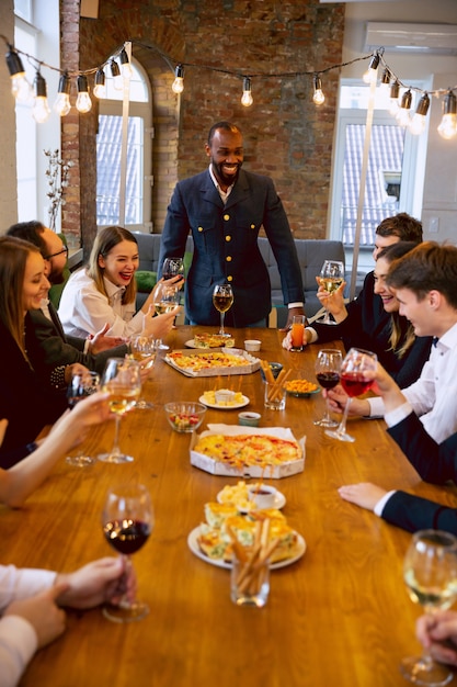 Happy co-workers celebrating while company party, corporate event. young caucasian people in business attire talking, drinking wine. concept of office culture, teamwork, friendship, holidays, weekend.