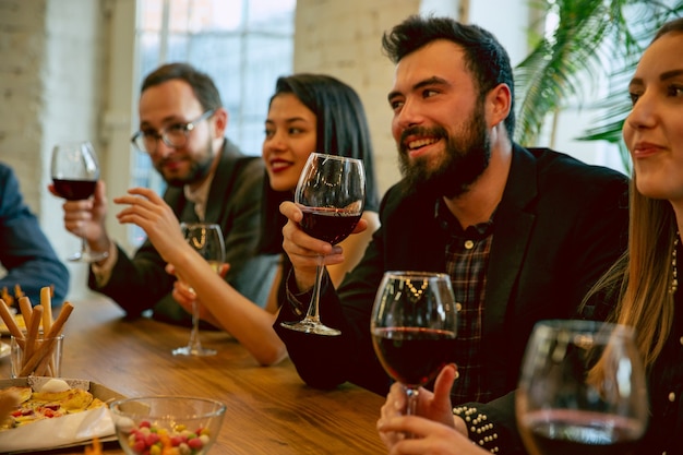 Happy co-workers celebrating while company party, corporate event. Young caucasian people in business attire talking, drinking wine. Concept of office culture, teamwork, friendship, holidays, weekend.