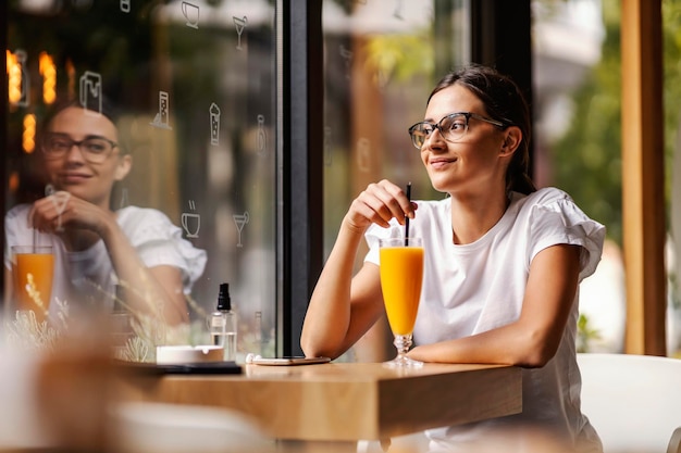 A happy college girl sitting in the cafeteria at her break and having fresh orange juice