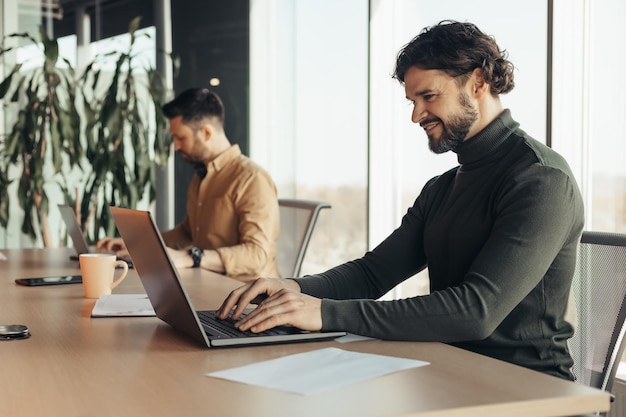 Happy company employee using laptop working next to male colleague at open space office