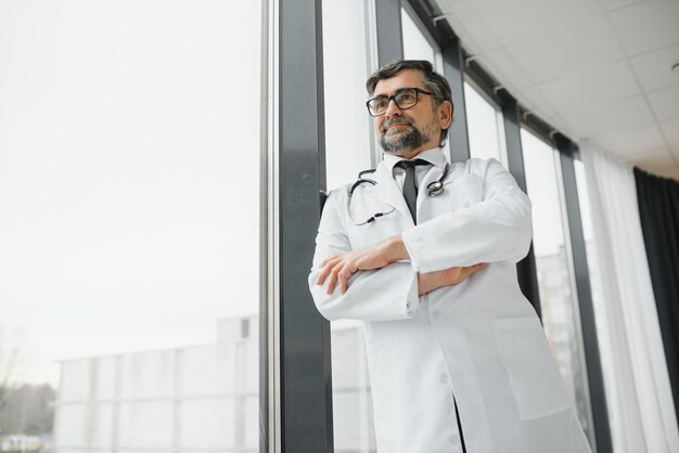 Happy confident bearded old professional doctor standing Smiling senior adult physician reliable successful therapist wearing white lab coat and stethoscope portrait