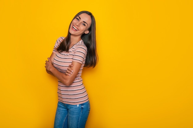 Happy confident beautiful young brunette woman in a t-shirt is posing and having fun isolated on the yellow background