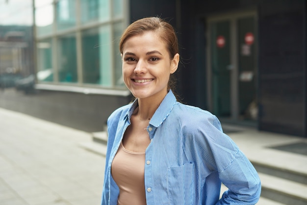 Happy confident business woman walking out of modern office center. Portrait of successful enterpreneur in smart casual outdoors.