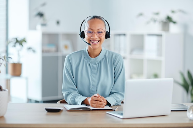 Happy and confident call center agent sitting in front of a laptop while wearing a headset in an office Portrait of a cheerful saleswoman using web chat to assist customer sales and service support