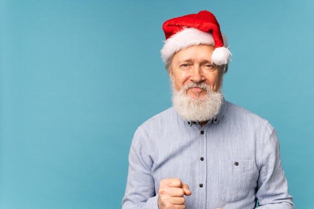 Счастливый уверенный в себе крутой старый бородатый победитель Санта-Клауса поднимает кулак, празднуя триумф и успех на синем фоне с копировальным пространством