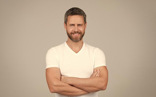 Happy confident man smile keeping arms crossed in white tshirt grey background guy