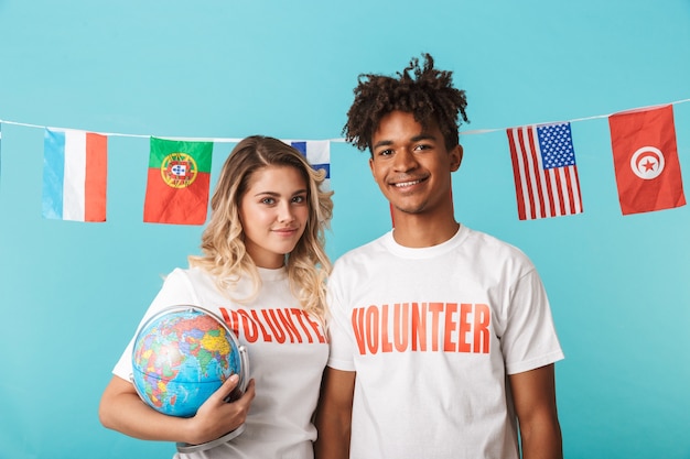 Happy confident multiethnic couple wearing volunteers t-shirt standing isolated over blue wall
