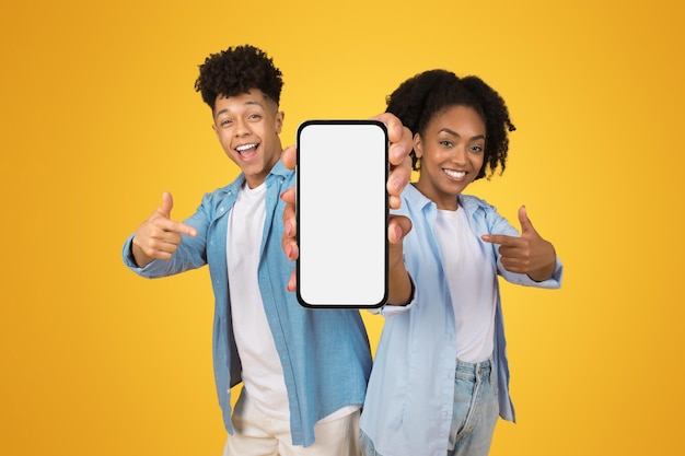 Happy confident young african american man and woman in casual point fingers at smartphone