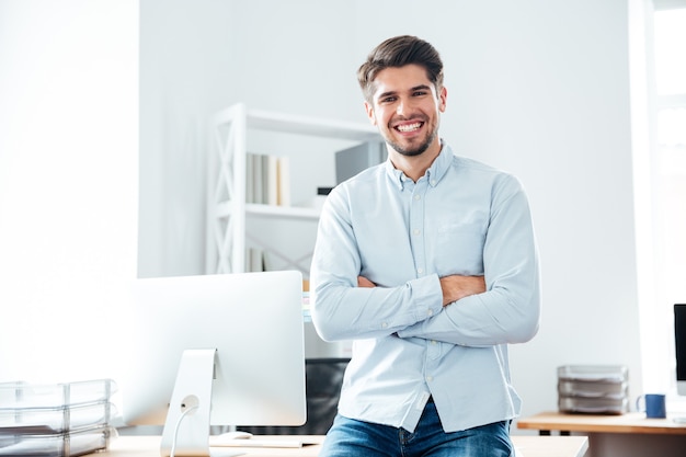 Happy confident young businessman standing with arms crossed in office