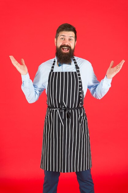 Happy to cook for you. Bearded man chef cooking. Hipster cooking home or restaurant. Modern cafe concept. Cooking modern meals. Man with beard cook hipster apron. Hipster chef cook red background.