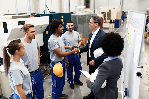 Felice manager aziendale che fa un giro in una fabbrica e stringe la mano a un lavoratore afroamericano