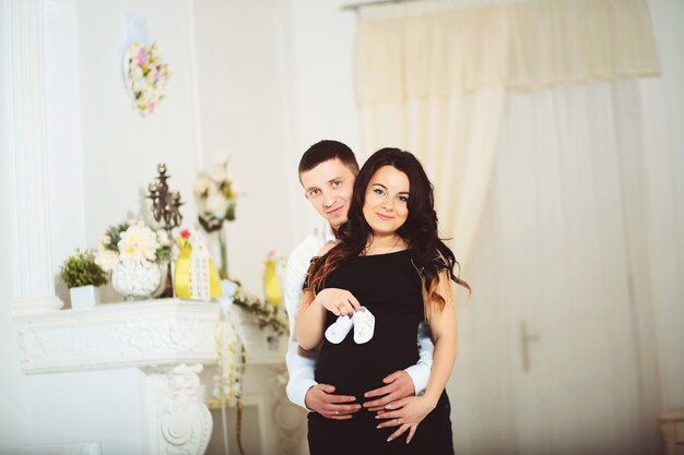 Happy couple awaiting baby, beautiful pregnant woman and her cheerful husband holding in hands cute tiny boots for their future child, new life concept