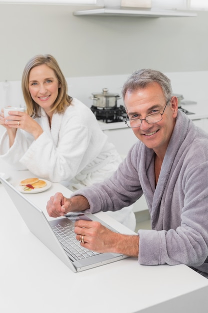 Happy couple in bathrobe doing online shopping at home