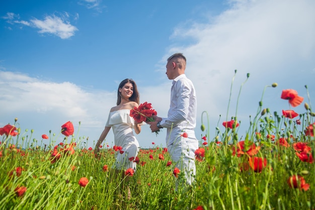 Happy couple breathing fresh air in a field with red poppy flowers, romantic date.