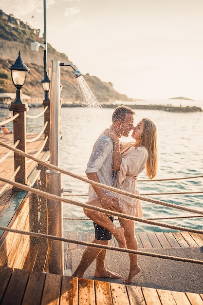 Happy couple by the sea A guy and a girl are under the shower on an openair pier Happy couple on vacation Man and woman by the sea