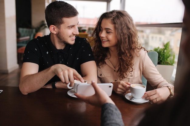 Happy couple in cafe look into smartphone and smile Woman show to man and woman something in phone Man put finger on screen and smile