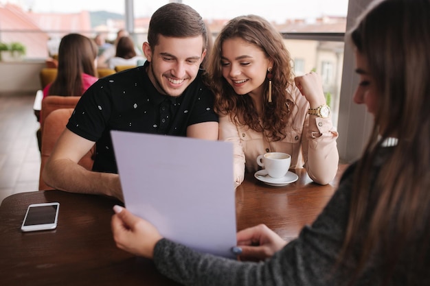Счастливая пара в кафе встречается с деловой женщиной Женщина показывает мужчине и женщине что-то на документах