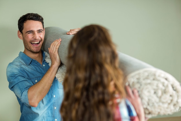 Happy couple carrying rolled up rug in their new house