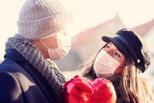 Счастливая пара празднует день святого валентина в масках во время пандемии covid-19 в городе