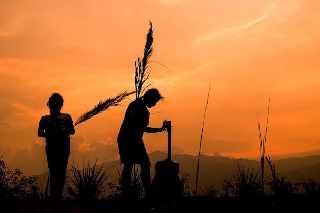 夕日、シルエットで牧草地で遊ぶ幸せなカップルの子供たち