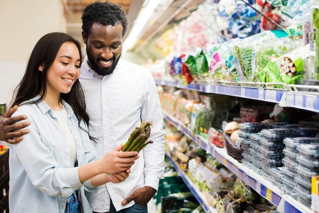 Счастливая пара, выбирая спаржу в продуктовом магазине