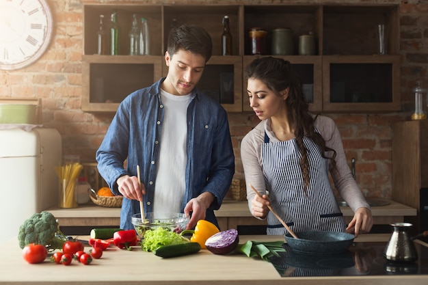 自宅のロフトキッチンで一緒に健康的な夕食を調理する幸せなカップル。野菜サラダの準備。