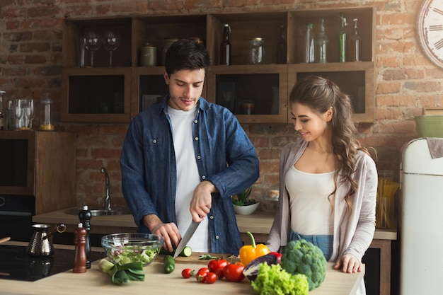 Coppia felice che cucina insieme cibo sano nella loro cucina soppalcata a casa. preparazione insalata di verdure, copia spazio