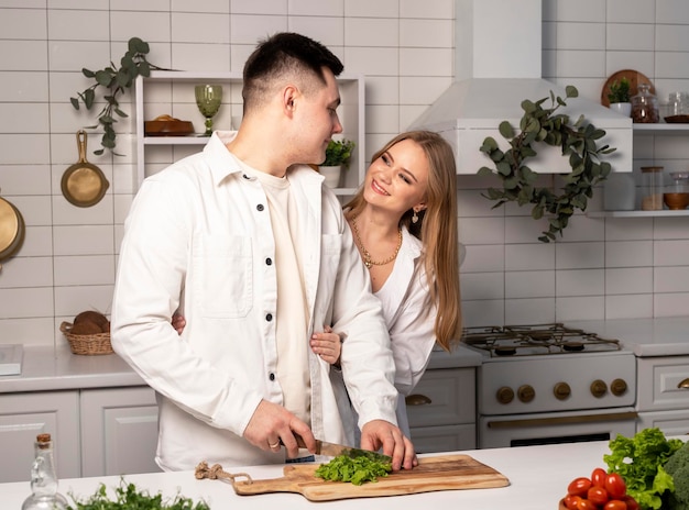 Happy couple cooking home man making vegetables salad in white scandi kitchen vegan food or healthy