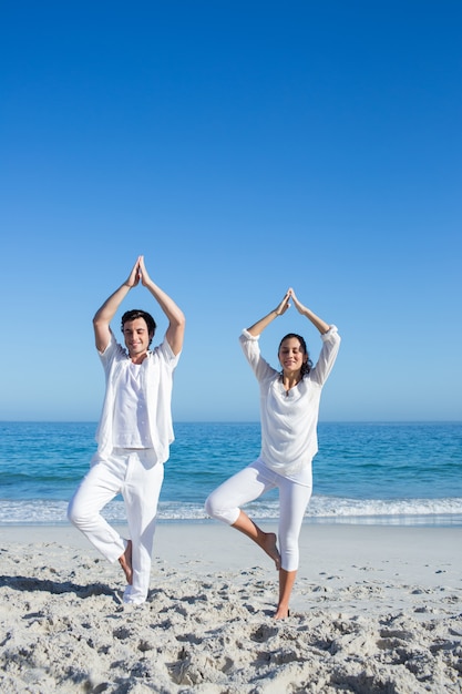 Happy couple doing yoga beside the water