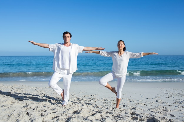 Happy couple doing yoga beside the water