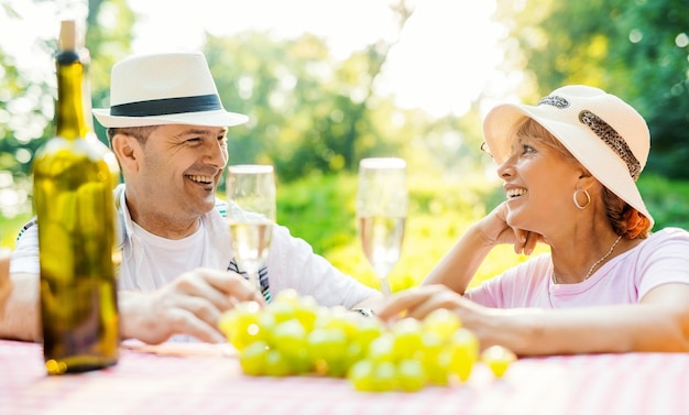 Happy couple drinking white wine on a picnic smiling at each other on a sunny day