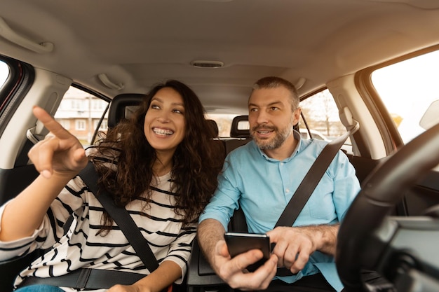 Happy couple driving car and using cell phone