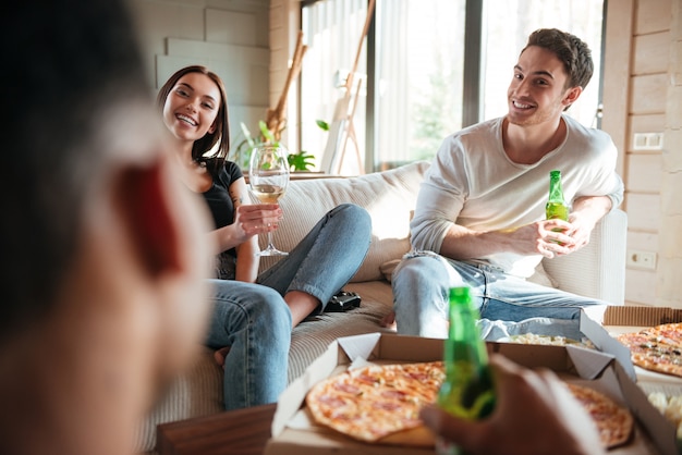 Happy couple eating pizza, drinking beer and wine with friends