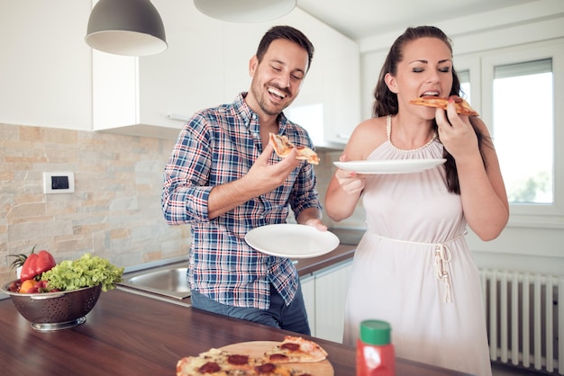 Happy couple eating pizza at their kitchen