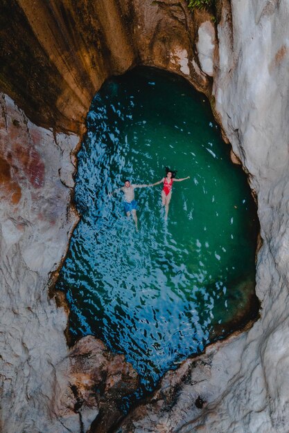 Happy couple floating in waterfall lake overhead top view