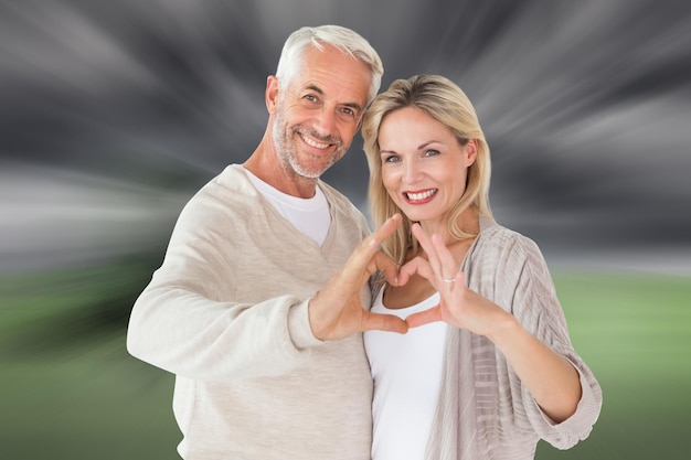 Happy couple forming heart shape with hands against misty green landscape
