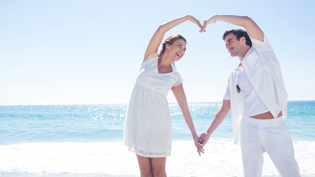 해변에서 자신의 손으로 하트 모양을 형성하는 행복 한 커플