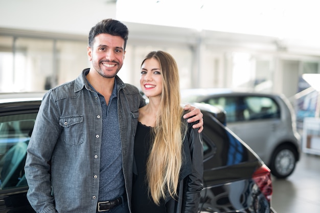 Happy couple in front of their new car in a showroom