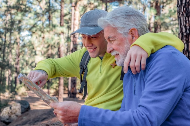 Happy couple of grandfather and teenager grandson hiking in the mountains rest checking the map Healthy lifestyle together in the woods Adventureisageless