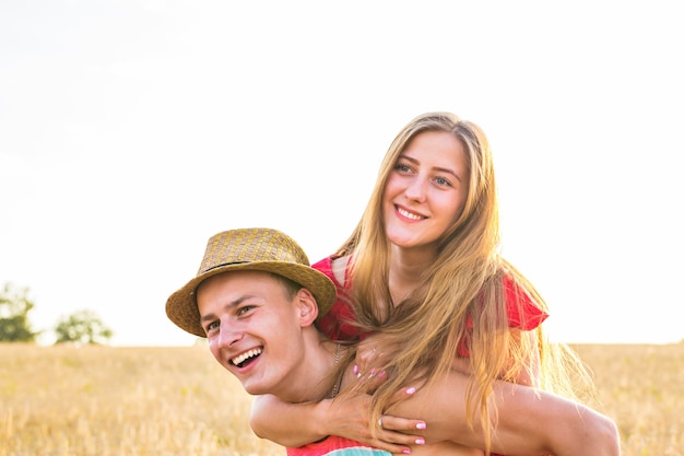 Happy Couple Having Fun Outdoors on wheat field over sunset. Laughing Joyful Family together. Freedom Concept. Piggyback