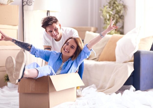 Happy couple having fun and riding in cardboard boxes at new home