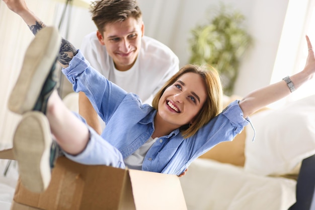 Happy couple having fun and riding in cardboard boxes at new home