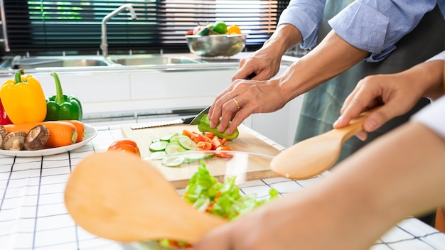 Coppie felici che hanno divertimento in piedi in cucina a casa a preparare insalata di verdure