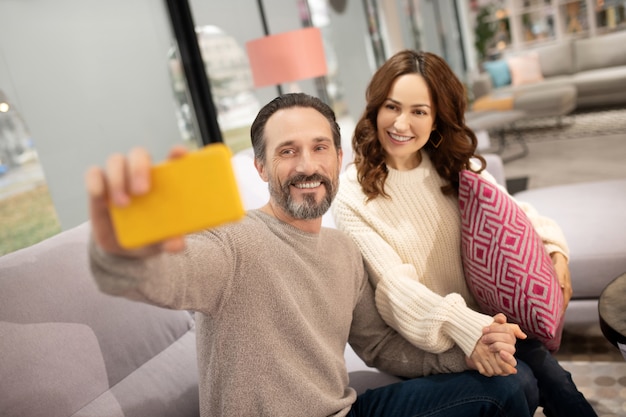 Happy couple having good time in the furniture salon making selfie