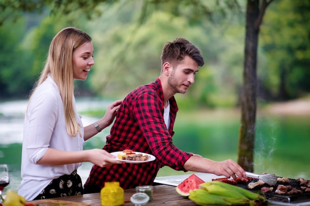 happy couple having picnic french dinner party outdoor during summer holiday vacation  near the river at beautiful nature