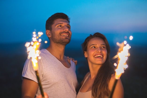 The happy couple hold a firework sticks. evening night time